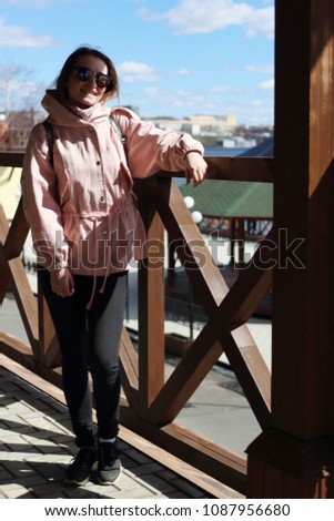 stunningly slender blonde in a pink spring jacket on the porch. A beautiful girl with slender legs on the veranda of a wooden building overlooking the embankment of the Izhevsk pond. Izhevsk, Russia