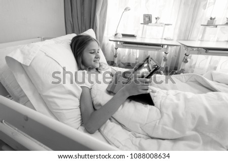 Black and white portrait of teen girl lying in bed and using digital tablet computer