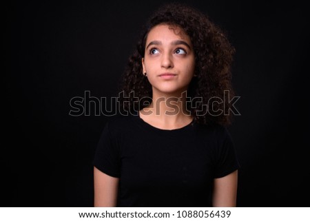 Studio shot of young beautiful Persian teenage girl with curly hair against black background