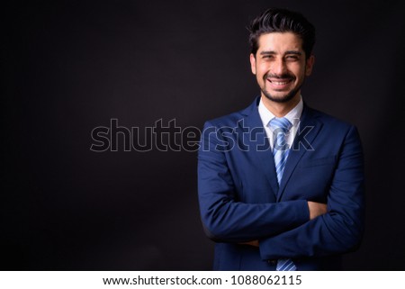 Studio shot of young handsome bearded Persian businessman against black background
