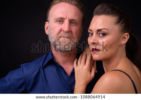 Studio shot of mature handsome bearded man and mature beautiful woman together against black background
