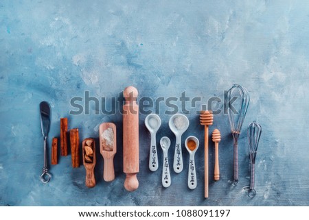 Measuring spoons, wooden scoops, whisks, rolling pin, honey spoons, sugar and cinnamon on a blue concrete background. Baking tools and ingredients concept flat lay with copy space.