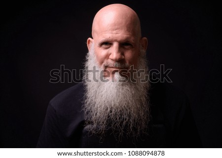 Studio shot of mature bald bearded man against black background
