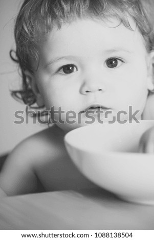 Portrait of interesting small cute baby boy with blonde curly hair and round cheecks and green plate closeup, vertical picture
