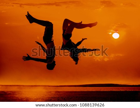 Silhouette of couple  happy young people fallen down on water on background of sunset beach and sea