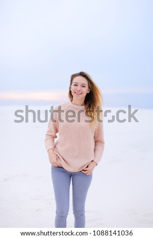 Happy blonde girl wearing pink sweater and jeans standing in white winter background. Concept of seasonal inspiration and photo session.