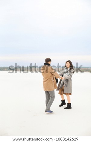 Gladden man and woman going on snow and holding hands, wearing coats and scarfs. Concept of monophonic winter background and happy couple.