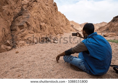 man sits on the ground in a rocky canyon and takes pictures on his smartphone the unsurpassed landscapes of the Egyptian mountains