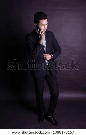 serious young man talking on mobile phone in black suit, modern man. Studio photography.