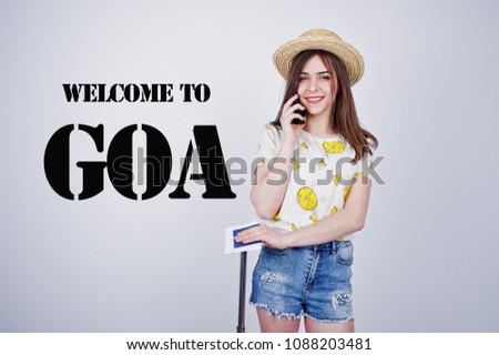 Girl tourist with bag, wear in shirt, shorts and hat, speaking on phone isolated on white. Welcome to Goa.