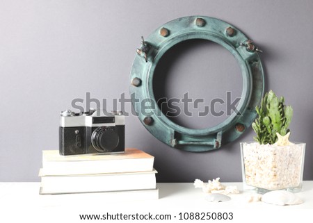 Blank ring porthole frame, plant cactus,old photocamera on the books on white table against the blue wall. Mockup with copy space.