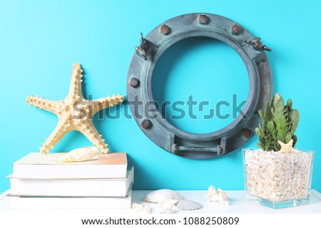 Blank ring porthole frame, plant cactus and starfish on books on white table against the blue wall. Mockup with copy space