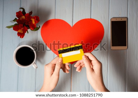 Woman's hand holds credit card over table, online shopping gifts through phone during coffee break. Concept of new technology. Flat lay