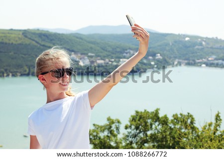 Pre teen girl taking selfie photo on the top of the mountain on the background lake. Summer view