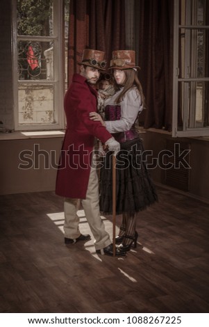 A man, a woman and a child, dressed in steampunk style clothes, posing in the interior against the background of large windows and screens