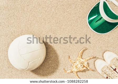 flat lay with volleyball ball, cap, sneakers and sea star on sand