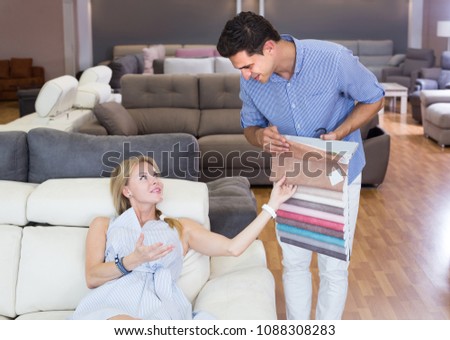 Salesman is showing colors for sofa to woman customer in home furnishings store
