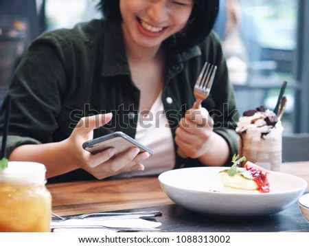 Asian woman joyful with food in restaurant,she eating delicious dessert dish and take a picture of food and herself.food blogger concept.