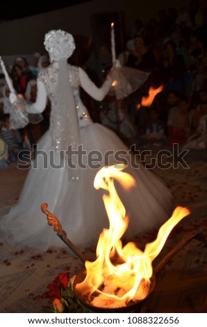 Dancing back to the viewer, the bride in a white dress and turban with a flame of fire on a large round candlestick at night