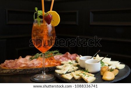 Traditional italian aperitif with proscioutto, mortadella sausage, cheese and aperol spritz drink on the wooden board with blurred food on the background Royalty-Free Stock Photo #1088336741