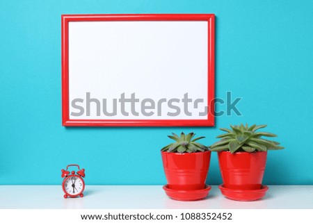 White empty canvas with red border near plant cactus isolated on white wooding book desk isolated on aquamarine background with copy space