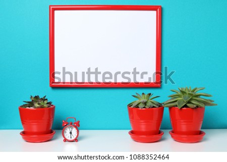 White empty canvas with red border near plant cactus miniature clock isolated on white wooding book desk isolated on aquamarine background with copy space