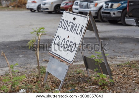 Metal sidewalk closed sign with blurred parking lot in background