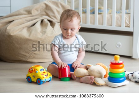 10 months old baby boy sitting on floor and playing with toys Royalty-Free Stock Photo #1088375600