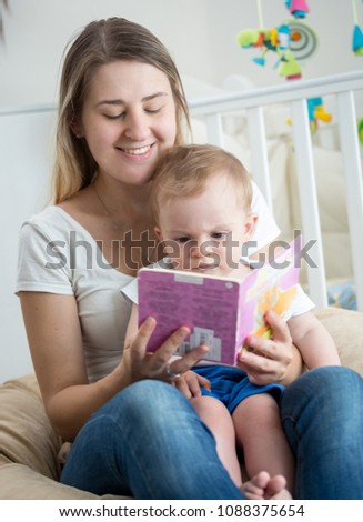 Happy smiling young woman reading book to her 10 months old baby son