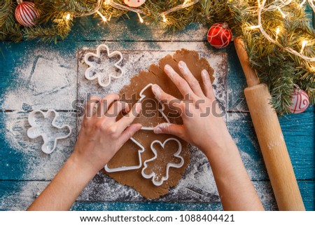 Photo of human hands, rolling pin, dough, spruce branches, garlands, biscuit molds