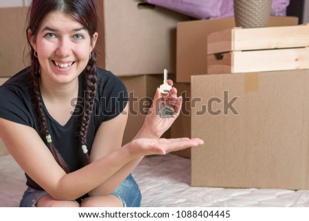 Image of young brunette with keys from apartment against blank wall