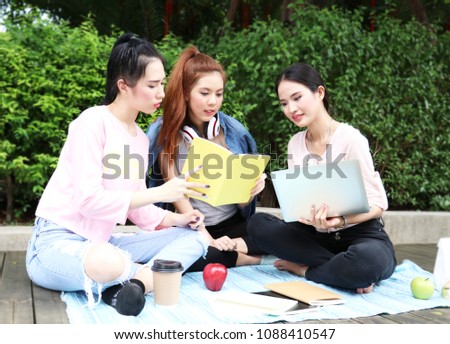 Asian women University Students smiling and sitting on the garden. Working and reading Outside Together in a park.