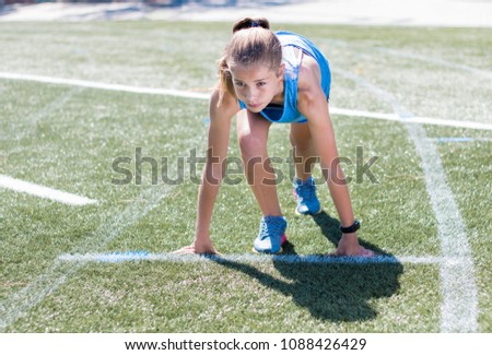 Sporty girl standing on her marks ready to run, looking focused and ready on running sports track.