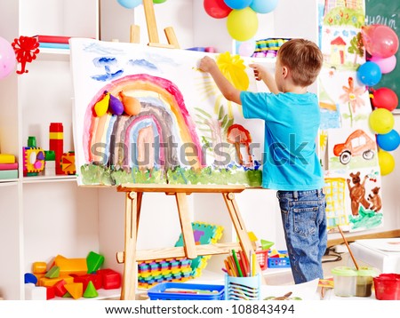 Child painting at easel in school. Education.