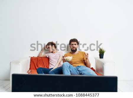 a man with popcorn watching TV, a woman turned away                               