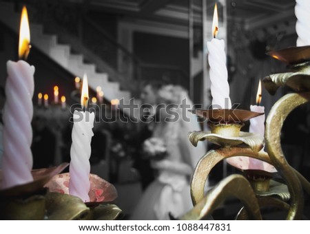 The couple goes to the altar. In the foreground candles, in the back - newlyweds. The bride holds a bouquet, the groom holds the bride in her hand. Black and white photo, colored candles