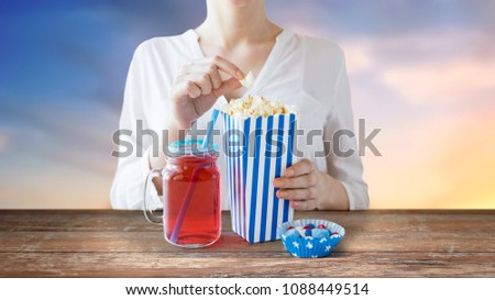 american independence day, celebration, patriotism and holidays concept - close up of woman eating popcorn with drink in glass mason jar and candies at 4th july party over evening sky background