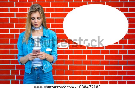 Young pretty woman type message - Female jeans fashion portrait - Teenager student holding mobile phone for sms next to brick wall background