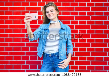 Young pretty woman taking selfie outdoors - Female summer fashion portrait - Teenager student holding mobile phone for selfi photo next to brick wall background