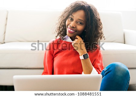 Attractive black young woman using a laptop while relaxing on a sofa at home