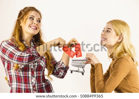 Two women holding shopping cart and sale percentage sign tag. Females enjoy buying cheap.