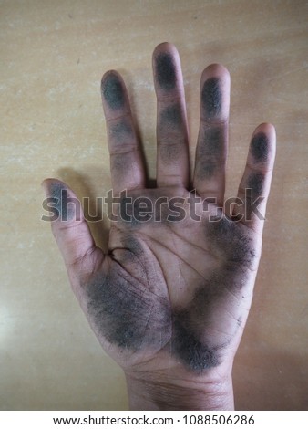 Left hand of Thai woman dirty because it touches black dust on wooden table.