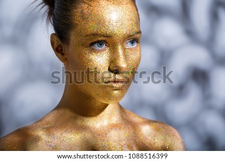 portrait of a beautiful young girl. Face painted with gold paint with glitter. abstract shadows on the background and on the model.