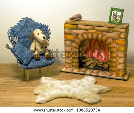A miniature knitted cute little dog toy sitting in a jeans puppet chair near a hand drawn sketch fireplace on black background. Background for postcards and children's books. Handmade, craft, hobby.