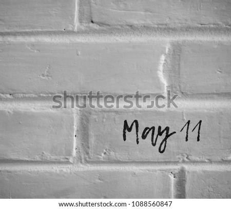 BLACK AND WHITE PHOTO OF " May 11 " WORDS WRITTEN ON WHITE PLAIN BRICK WALL