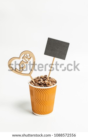 Grains of coffee in a yellow paper glass, a sign for writing and a beautiful heart with the word love