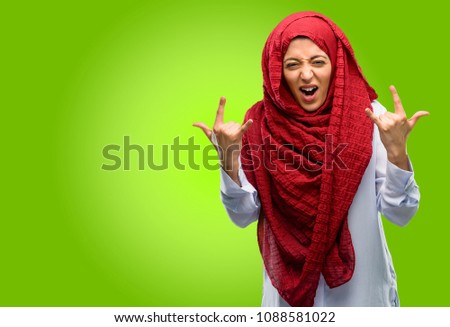 Young arab woman wearing hijab making rock symbol with hands, shouting and celebrating