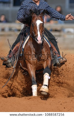 The front view of a rider sliding the horse in the sand.