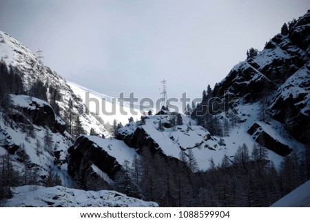 Summit of a mountain stones and snowy pines metal towers in northern Italy.