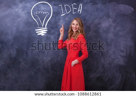 A young beautiful girl in a red dress shows a hand on a drawing. On a black board a lamp is drawn and the girl shows them a hand. Various human emotions, the body language.